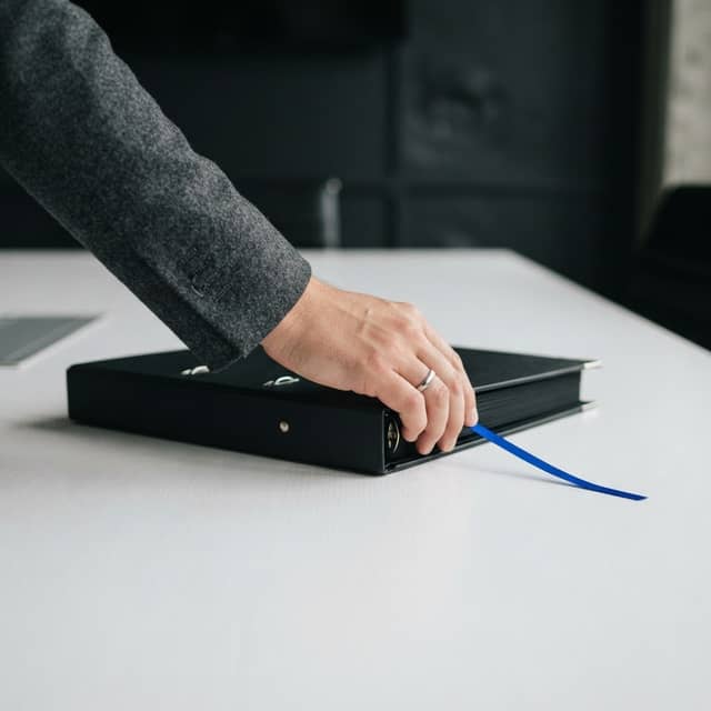 Professional hand adjusting a black binder with blue accent ribbon