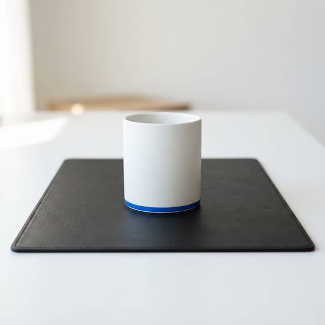 A single minimalist mug on a dark leather desk pad in a professional office setting