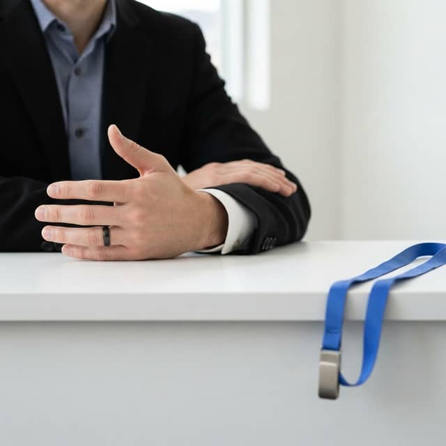 Professional hands in a blazer resting on a desk with a blue lanyard