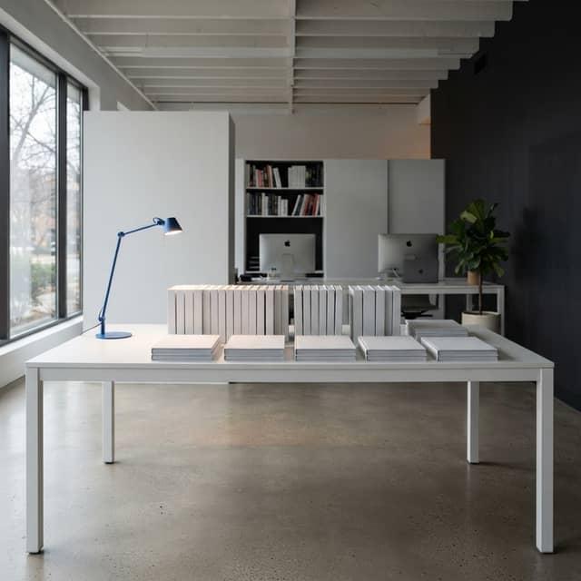 A minimalist studio workspace with a white table and a single electric blue desk lamp