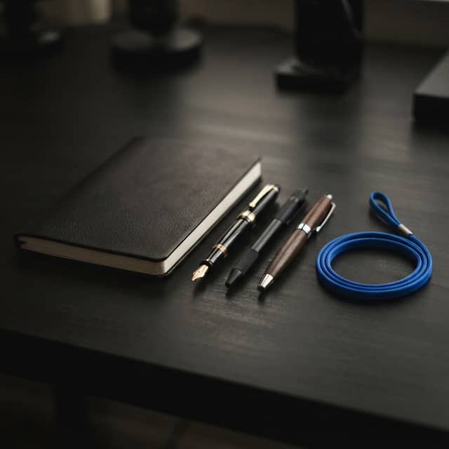 Minimalist notebook and pens on a dark desk with a blue lanyard